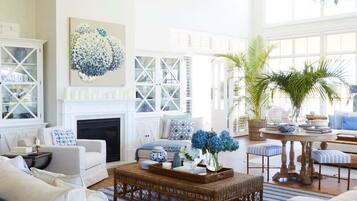 A spacious living room with a fireplace, a large chandelier, and a view of the outdoors.