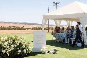 A tent with a sign reading 'LET'S WINE AND DINE' and a group of people seated at a table under the tent.