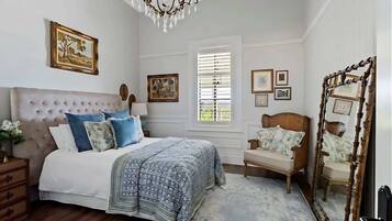 A bedroom with a tufted headboard, a bed with patterned bedding, a wooden chair, and a mirror with a wooden frame.