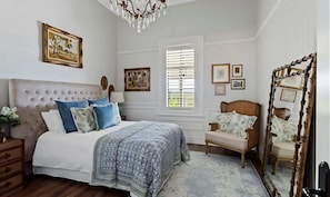 A bedroom with a tufted headboard, a bed with patterned bedding, a wooden chair, and a mirror with a wooden frame. - Hamptons Farm Estate—Luxe Retreat & Elegant Events (Wongamine)