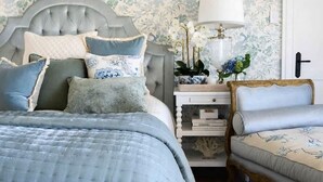 A bedroom with a tufted headboard, a bed with a quilted bedspread, a bedside table with a lamp, and a chair with floral upholstery. - Hamptons Farm Estate—Luxe Retreat & Elegant Events (Wongamine)