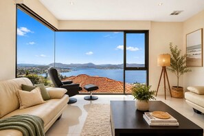 A modern living room with a large sliding glass door leading to a balcony with a scenic view of a coastal area.