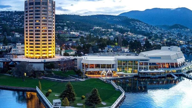 Ett högt hotell med flera våningar, utsikt över vattnet och en modern byggnadskomplex med stora fönster och utomhusområden med sittplatser.