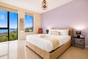 Un dormitorio amplio con una cama grande, una mesita de noche, una silla y vista al mar.