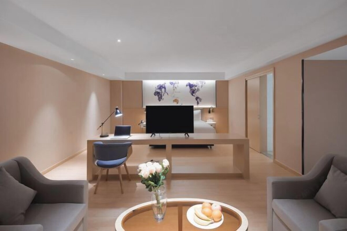A modern hotel lobby with a reception desk, a flat-screen TV, a vase with flowers, and two sofas.