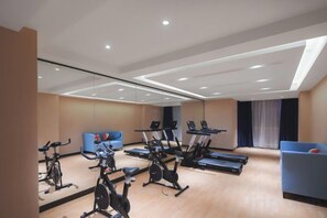 A gym with exercise bikes, treadmills, and a blue sofa. - Kyriad Marvelous Hotel (Suzhou Wujiang People's Square) (Suzhou)