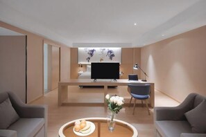 A modern hotel room with a central desk, a flat-screen TV, a dining area with a tray of bread, and a vase of flowers. - Kyriad Marvelous Hotel (Suzhou Wujiang People's Square) (Suzhou)