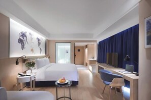 A modern hotel room with a large bed, a desk, a chair, and a small table with fruit. - Kyriad Marvelous Hotel (Suzhou Wujiang People's Square) (Suzhou)