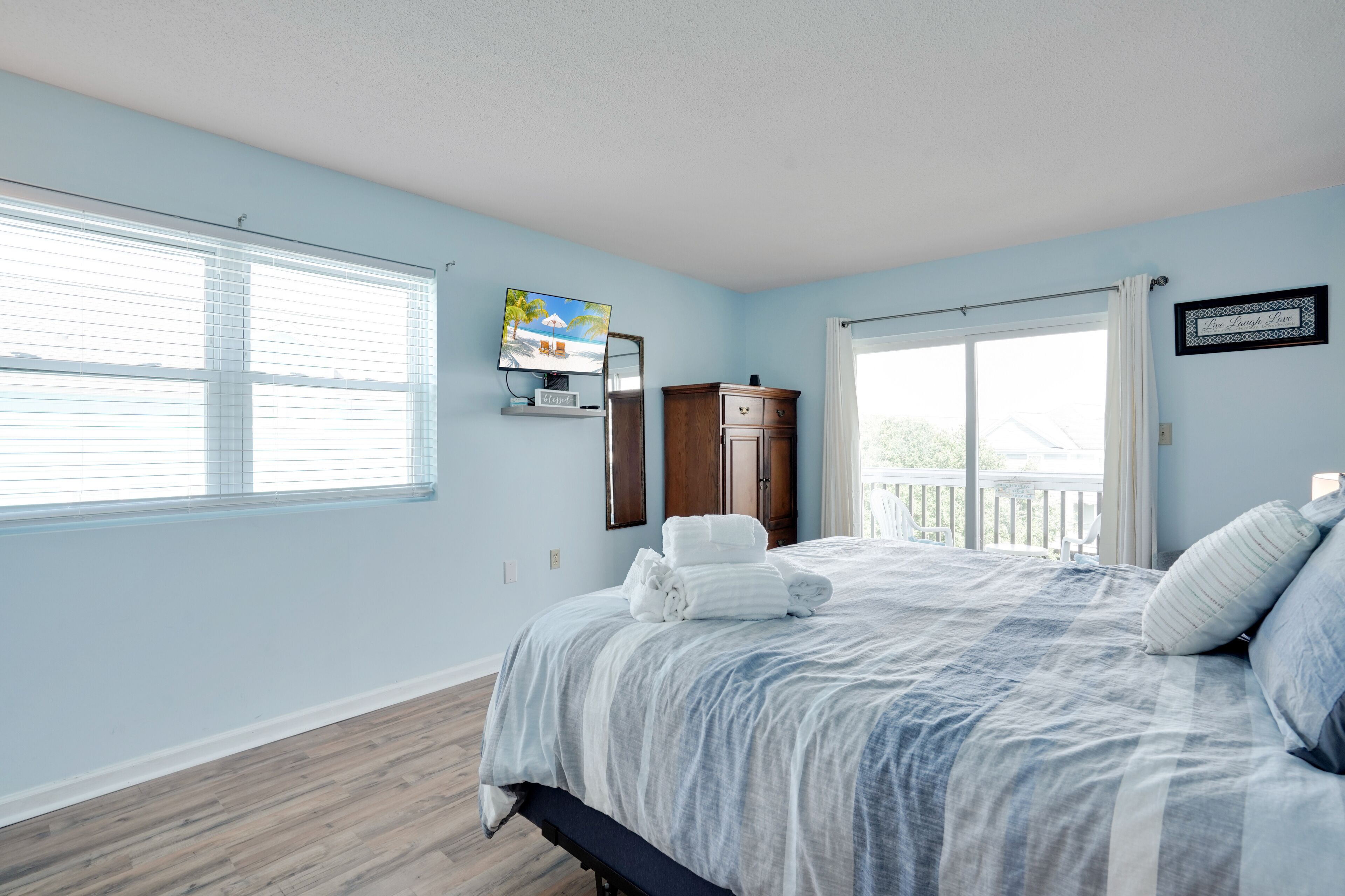 A bedroom with a bed, a TV, a wooden cabinet, and a window with blinds.