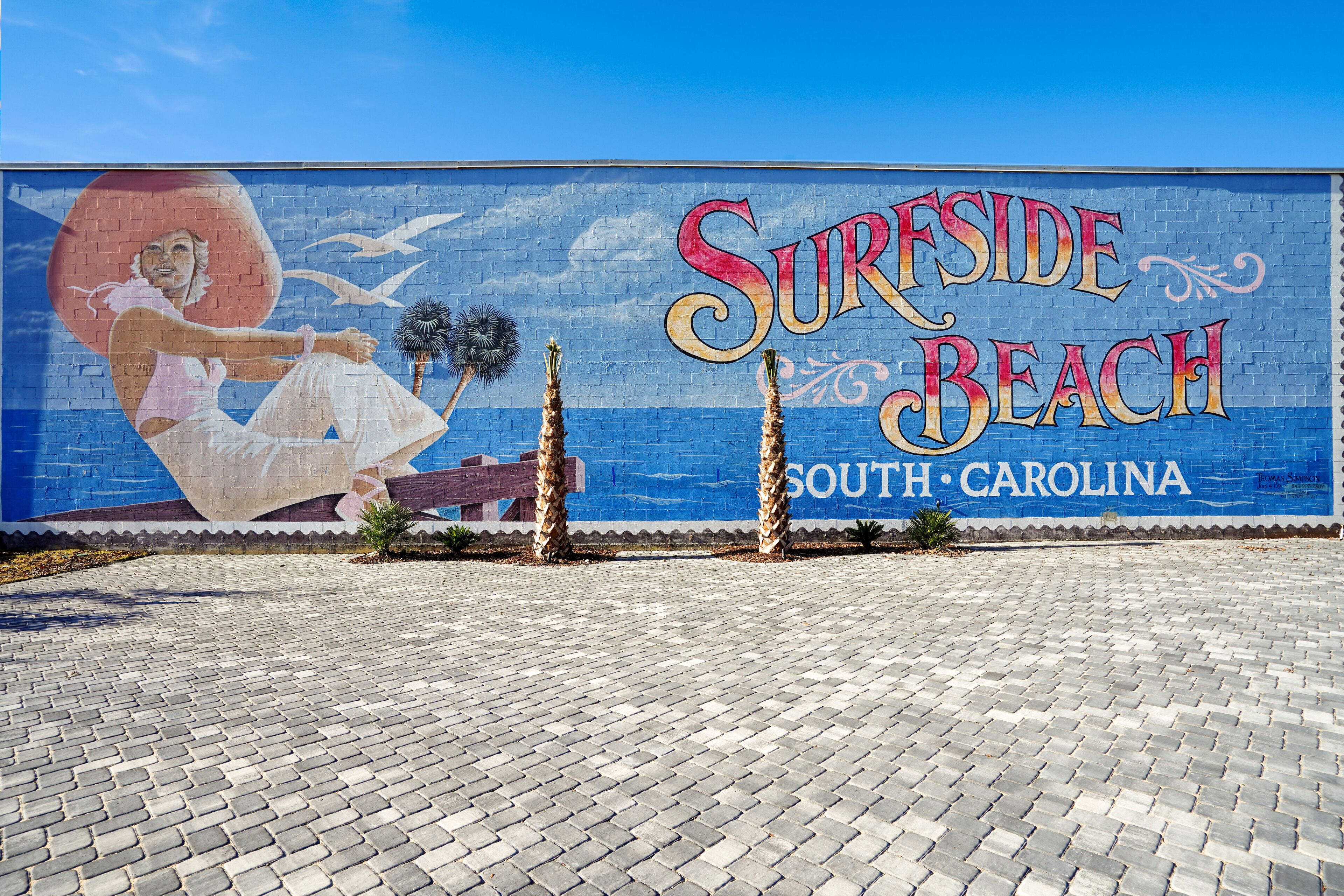 Een muurschildering met de tekst 'Surfside Beach South Carolina' en palmbomen.