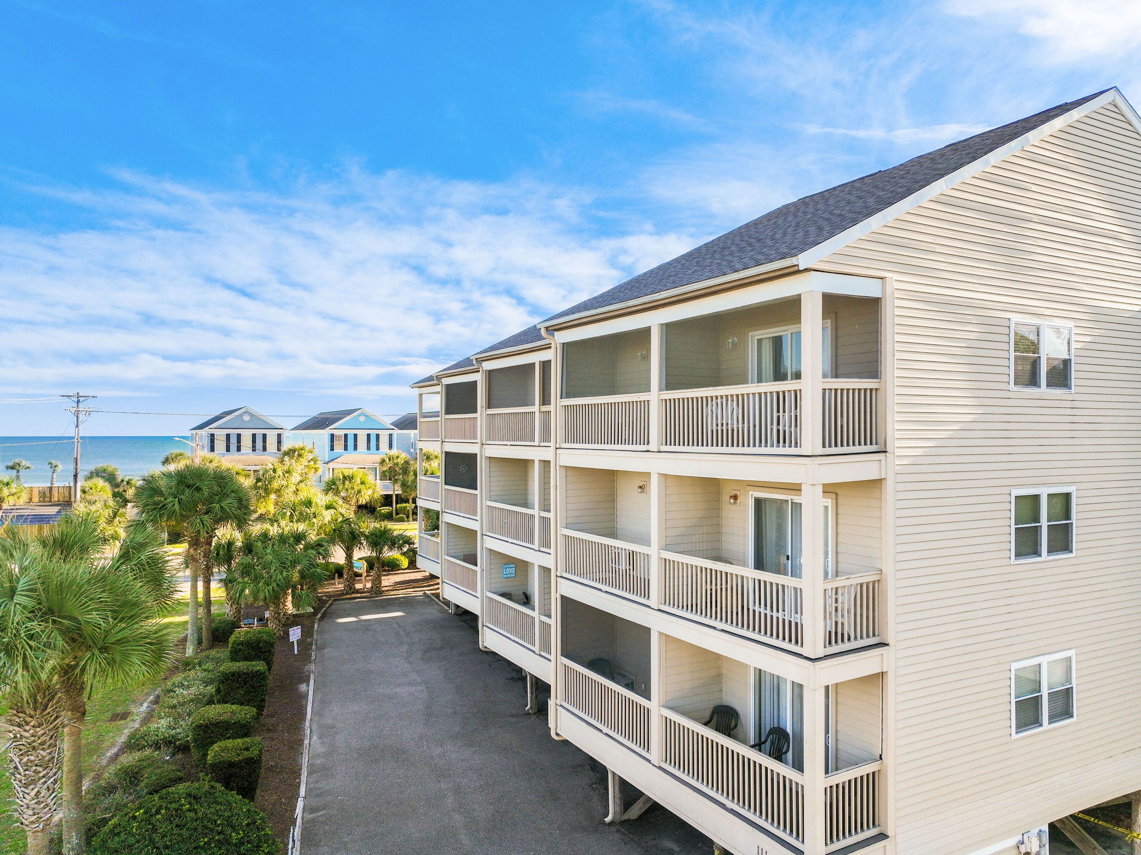 A multi-story building with balconies, a paved driveway, and a view of the ocean.