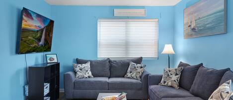 A living room with a blue wall, a grey sofa, a coffee table, a bookshelf, and a painting.
