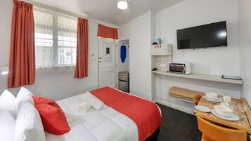 A hotel room with a bed, a TV, a microwave, a small fridge, a desk with a chair, and a dining table set for two.