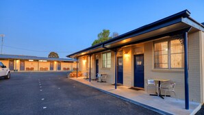 Un motel con una hilera de habitaciones, asientos al aire libre y un estacionamiento.