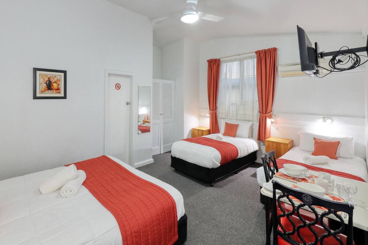 A hotel room with two beds, a desk with a chair, a television, and a window with curtains.