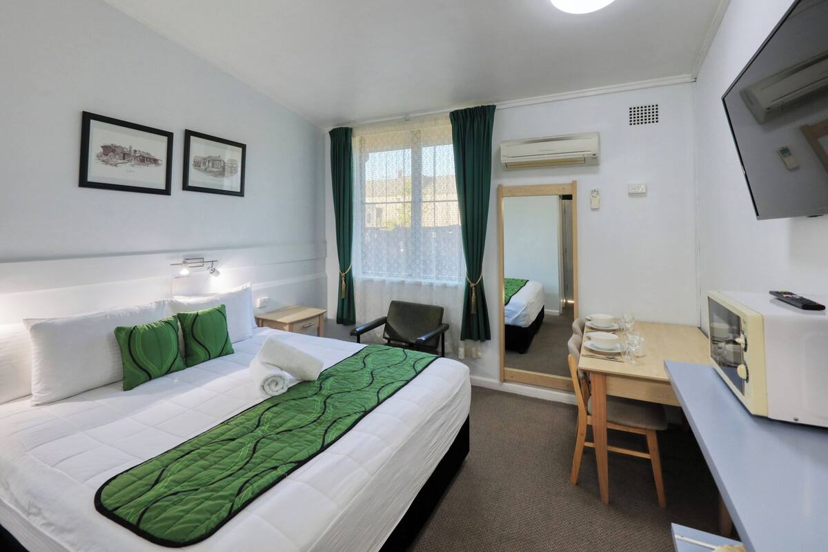 A hotel room with a bed, a desk, a chair, a TV, and a window with curtains.