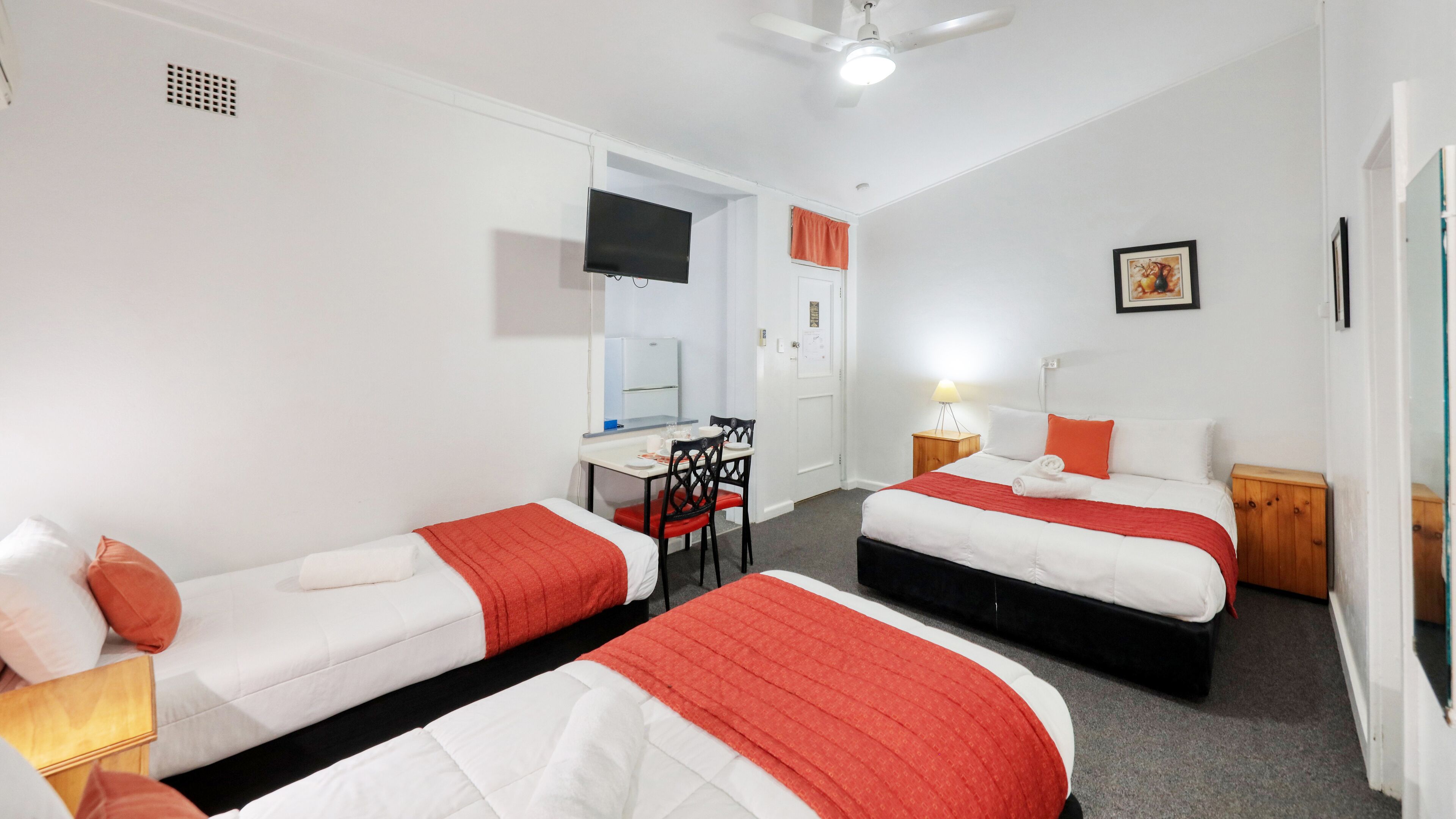A hotel room with two single beds, a desk with a chair, a TV, and a door.