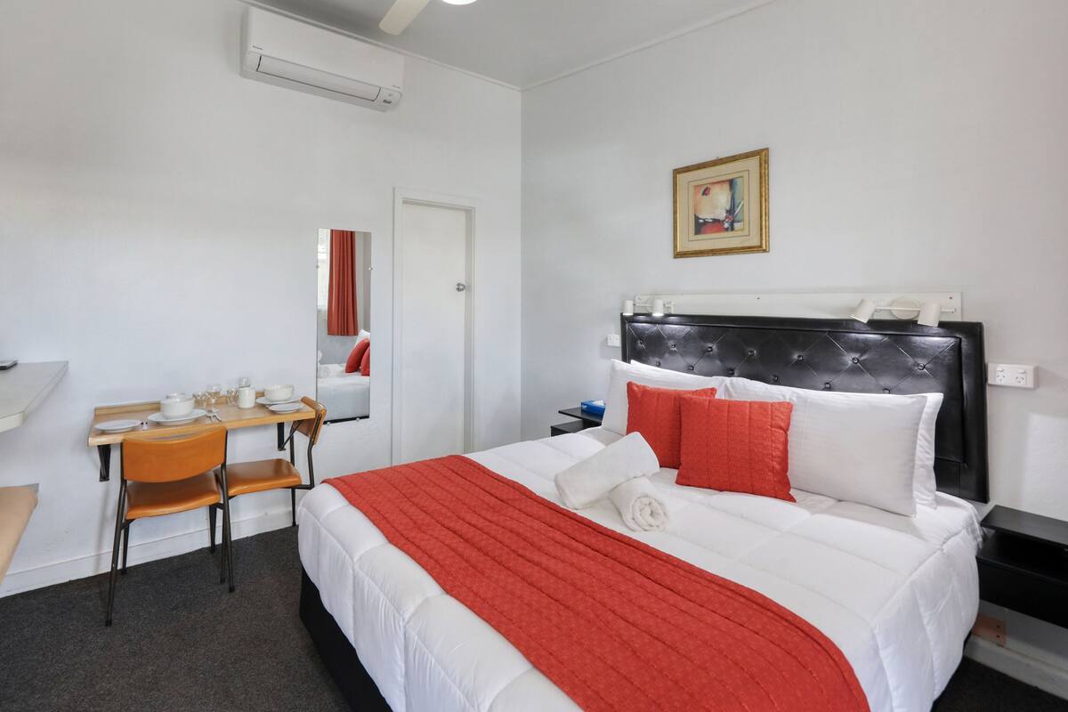 A hotel room with a bed, a desk with a chair, a microwave, and a painting on the wall.