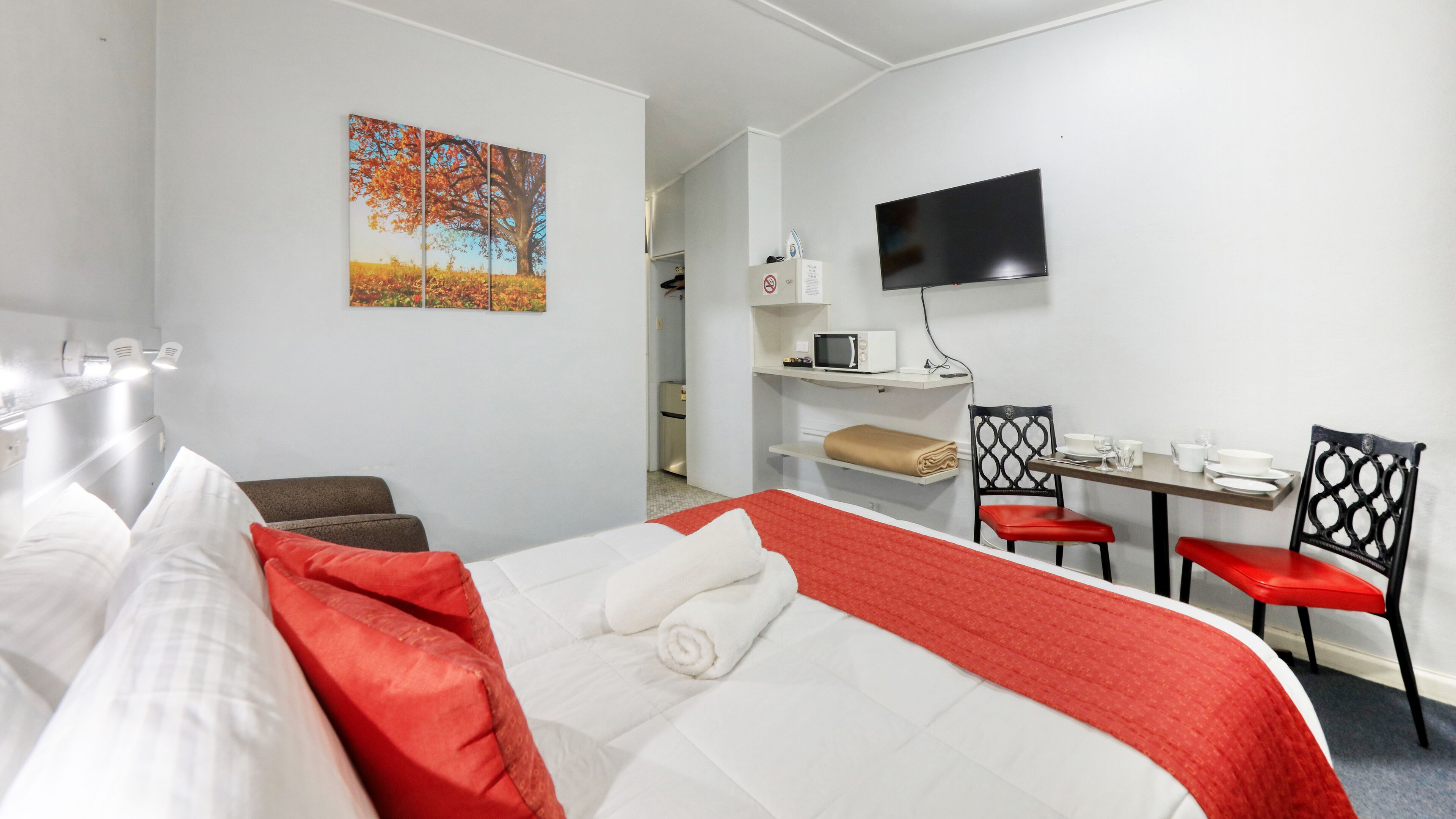 Una habitación de hotel con una cama, un escritorio con una silla, un televisor y un cuadro en la pared.