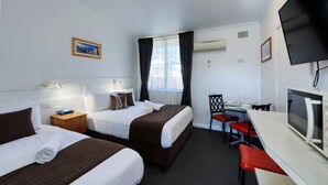 Habitación de hotel con dos camas, un escritorio, una silla, un televisor y una ventana con cortinas.