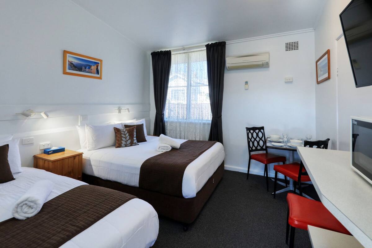 A hotel room with two beds, a desk, a chair, a television, and a window with curtains.