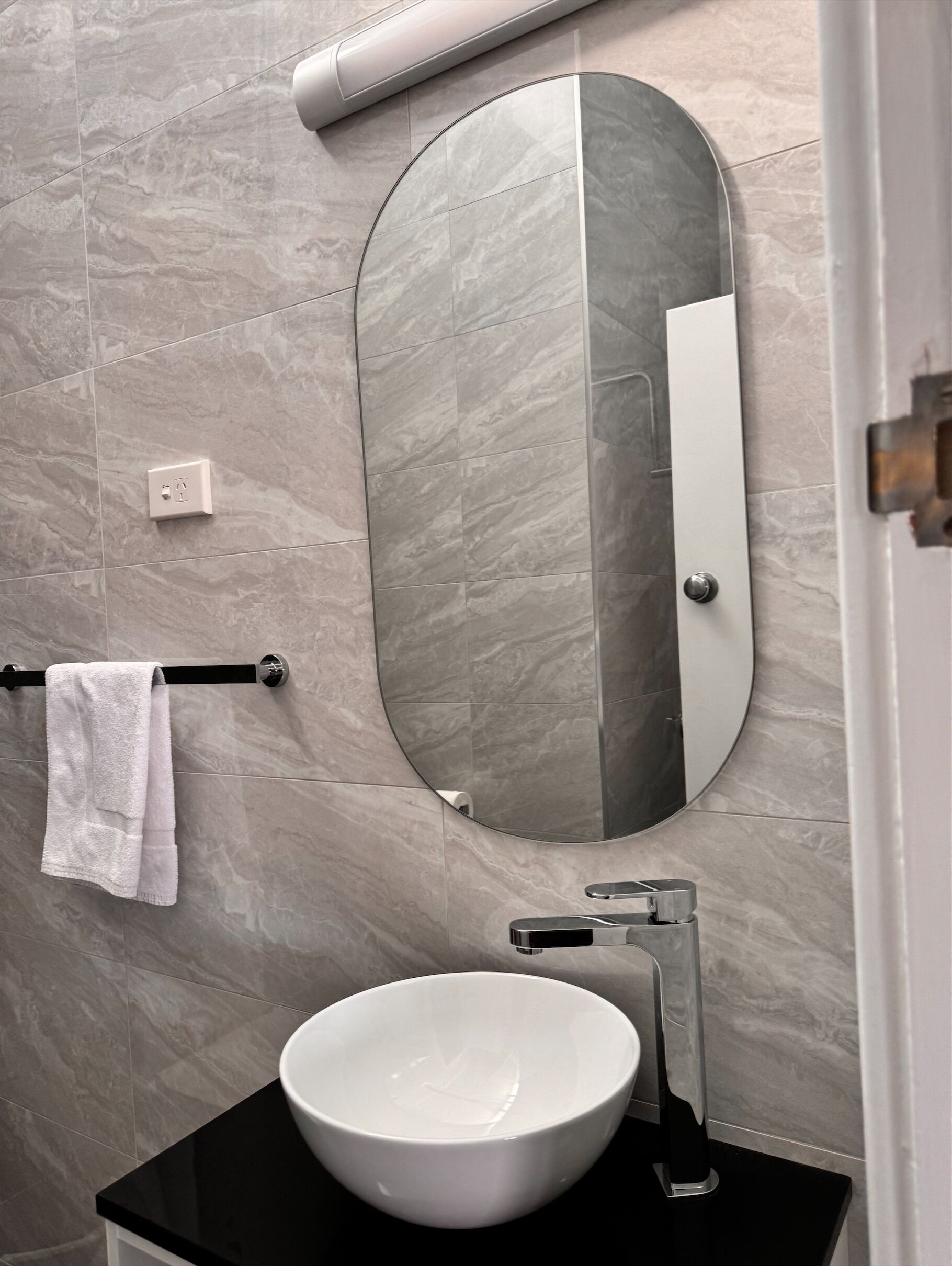 A bathroom with a round mirror, a white sink, and a towel rack.