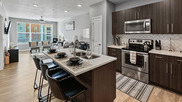 A modern kitchen with a central island, stainless steel appliances, and a view of the city through large windows.