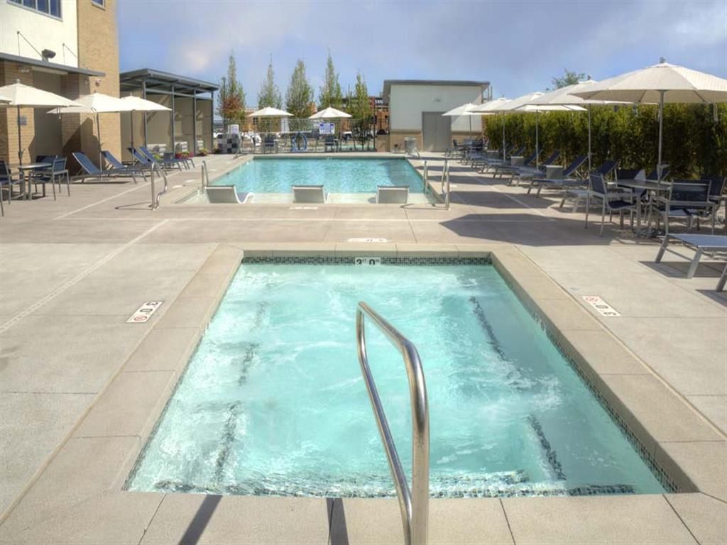 A pool area with two pools, lounge chairs, umbrellas, and a clear sky.