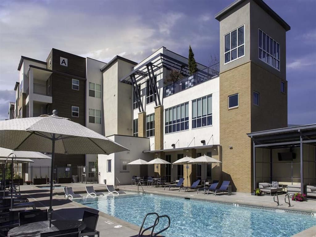 A modern building with a swimming pool, lounge chairs, and umbrellas.