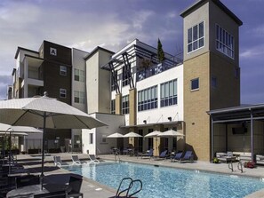 A modern building with a swimming pool, lounge chairs, and umbrellas.