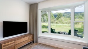 Un salon moderne doté d’un grand téléviseur à écran plat, de meubles en bois et offrant une vue sur un paysage verdoyant grâce à une grande baie vitrée.