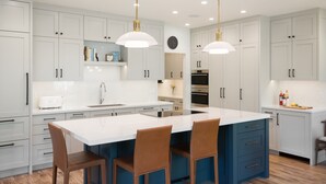 Une cuisine moderne avec des meubles blancs, un îlot central doté de chaises, des luminaires suspendus et un four encastré.