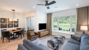 Un salon moderne comprenant un coin repas, un téléviseur à écran plat et une grande fenêtre donnant sur un paysage verdoyant.