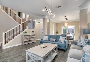 A spacious living room with a staircase, a blue sofa set, a coffee table, and a chandelier. - Modern Home w Heated Pool Game Rm sleeps12-15 near DFW & Gaylord hotel (Flower Mound)