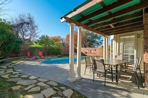A covered patio with a pool, stone pathway, and outdoor furniture.