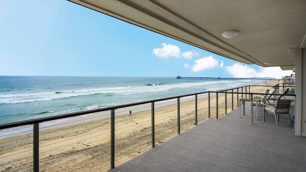 A beach view from a covered balcony with a railing, a pier in the distance, and a sandy beach. - Gorgeous Beachfront  Condo (Imperial Beach)