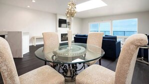 A modern living room with a glass-top dining table surrounded by patterned chairs, a decorative vase, and a view of the ocean through large windows. - Gorgeous Beachfront  Condo (Imperial Beach)