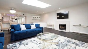 A modern living room with a blue sofa, a glass coffee table, a fireplace, and a TV mounted on the wall. - Gorgeous Beachfront  Condo (Imperial Beach)
