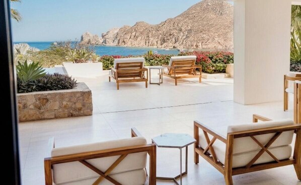 A terrace with wooden furniture, a table, and a view of the sea and mountains.