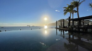 Une piscine à débordement offrant une vue sur l’océan et les palmiers.