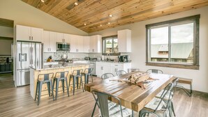 A modern kitchen with wooden ceiling beams, white cabinets, and a central island with bar stools.