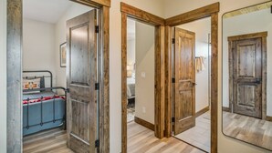 A hallway with wooden doors leading to a bedroom with a bed and a small table.