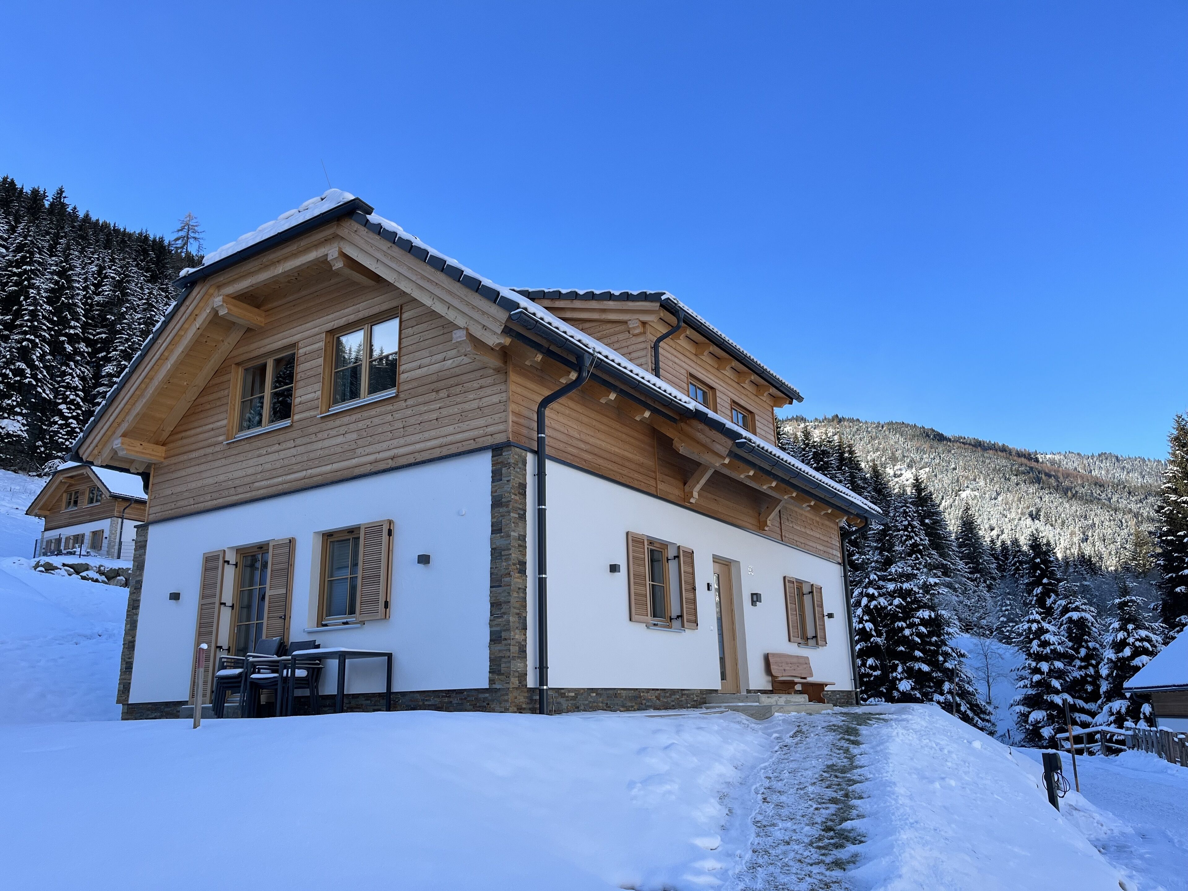 A two-story wooden house with a stone foundation, a covered porch, and a snow-covered landscape.