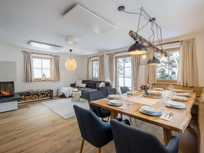 Een moderne woonkamer met een open haard, een eethoek met een houten tafel voor vier personen, en een gezellige zithoek met een bank en een salontafel.
