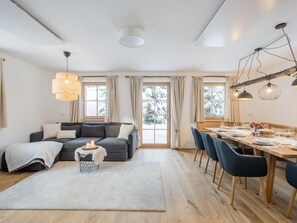 Een moderne woonkamer met een bank, een eettafel gedekt voor twee personen en een groot raam met gordijnen.