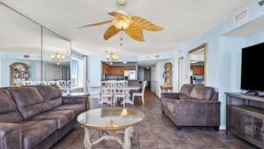 A spacious living room with a brown leather sofa, a glass coffee table, and a ceiling fan with a leaf design.