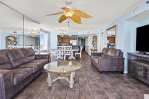 A spacious living room with a brown leather sofa, a glass coffee table, and a ceiling fan with a leaf design. - Premiere oceanfront condo w/indoor/outdoor pools, lazy river, fitness center, hot tubs--family fun (North Myrtle Beach)