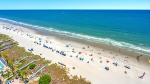 A beach with rows of sun loungers and umbrellas, a lifeguard tower, and a clear view of the ocean.