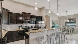 Una cocina moderna con armarios oscuros, electrodomésticos de acero inoxidable y una zona de bar con sillas blancas.