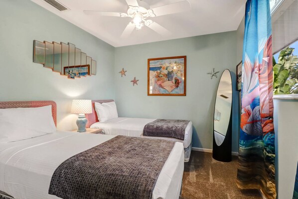A room with two beds, a ceiling fan, a painting, and a surfboard. - 250 1st St-a (Bonita Springs)